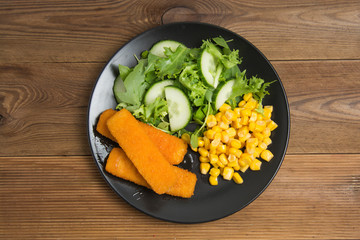 Fish fingers with green salad and corn. Healthy food for kids.
