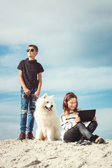 Happy 11 year old boy withhis dog breed Samoyed at the seashore against a blue sky close up. Best friends rest and have fun on vacation, play in the sand