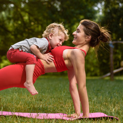 Fototapeta premium Young mother and little boy exercising on mat in park