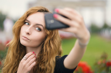 Naklejka premium Young redhead girl taking a selfie outdoors on sunny day.