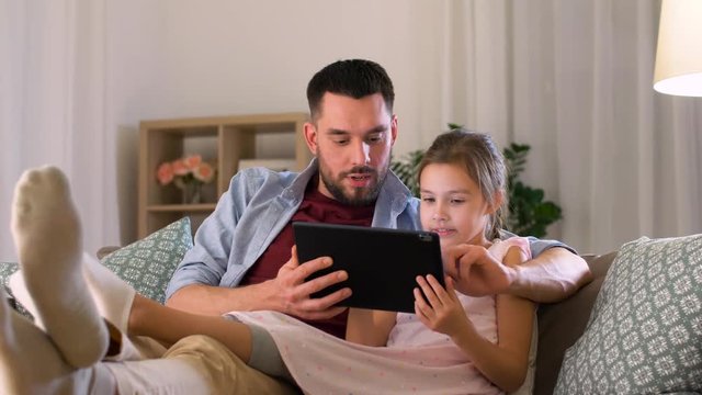 family, fatherhood and technology concept - happy father and little daughter with tablet pc computer at night at home