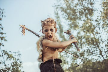 Caveman, manly boy with weapon aggressively shouting. Dramatic action photo of young primitive boy outdoors . Evolution survival concept. Calm boy outside standing in attack pose. Prehistoric tribal