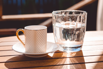 A cup of Turkish coffee and a glass of water on the wooden table on a terrace in a garden, coffee break, workplace, sunny day, chilling time, restaurant, cafe, 