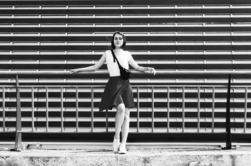 Black and white shot of Attractive young woman leaning back on fence in front of repetitive urban wall