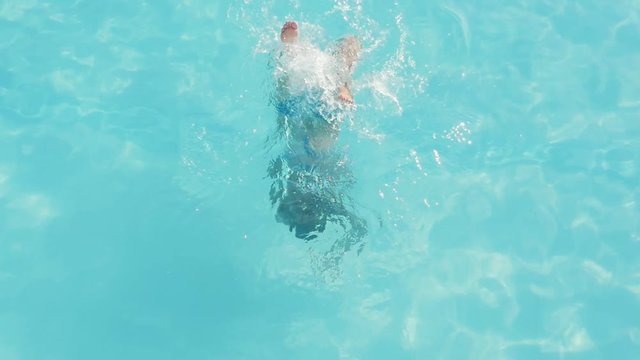  Exciting view of an entertaining blond woman in blue bikini moving down and touching the bottom of a swimming pool with celeste water in slow motion