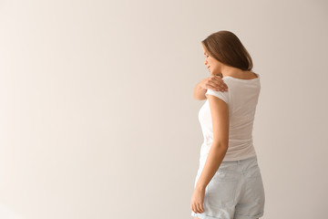 Young woman suffering from pain in shoulder on light background