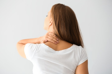 Young woman suffering from neck pain on light background