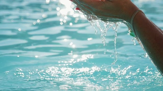  Inspiring view of two female hands raising shining water splashes over a wading pool outdoors with crystalline turquiose waters on sunset in summer