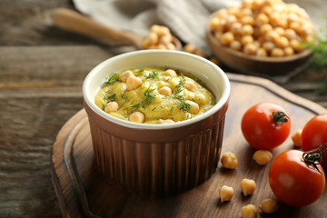 Bowl with tasty hummus on wooden board, closeup