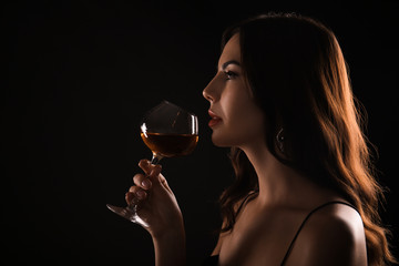 Beautiful young woman with glass of wine on dark background