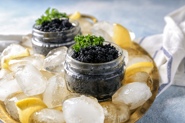 Jars with delicious black caviar and ice cubes on metal tray