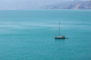 Fototapeta premium Mediterranean sea landscape with small yacht on calm water surface background texture aerial shot from above top point of nature cape rock