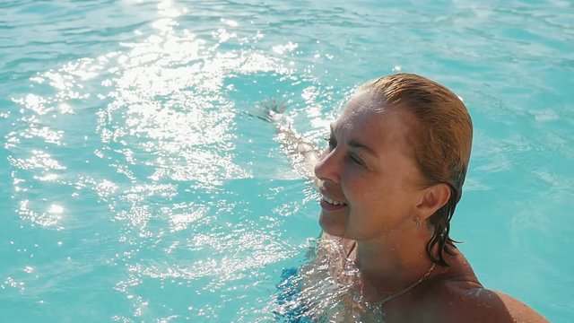  Sunny view of a happy blond woman relaxing, smiling and swimming in a padling pond on a sunny day in summer. She feels optimistic and relaxed.