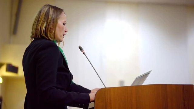 woman politician is speaking in large auditorium, reading her presentation and explaining program