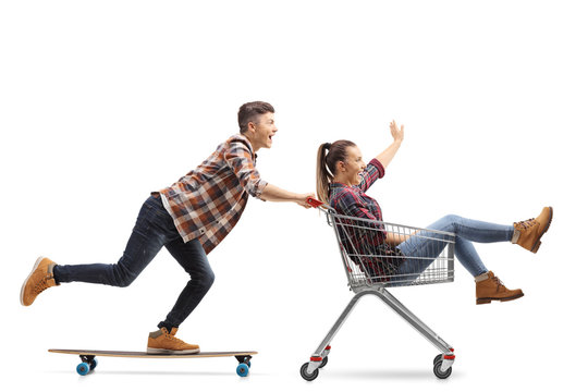 Young guy riding a longboard and pushing a girl in a shopping cart