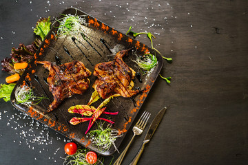 A dish with roasted quail meat with vegetables on black background