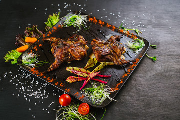 A dish with roasted quail meat with vegetables on black background