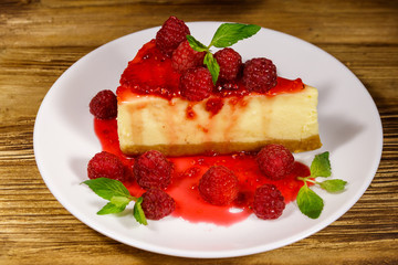 Piece of tasty New York cheesecake with raspberries and raspberry jam in a white plate on wooden table