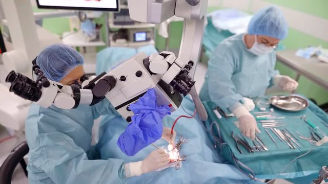 ent surgeon is operating ear of patient and installing a hearing prosthesis, watching through microscope