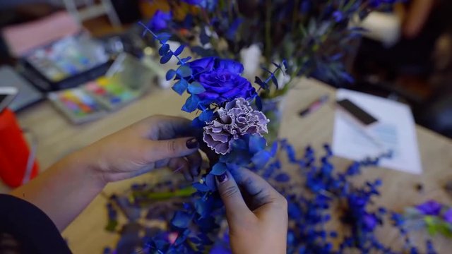 florist is making creative blue bouquet, rotating flowers in hands, painting by blue color, close-up