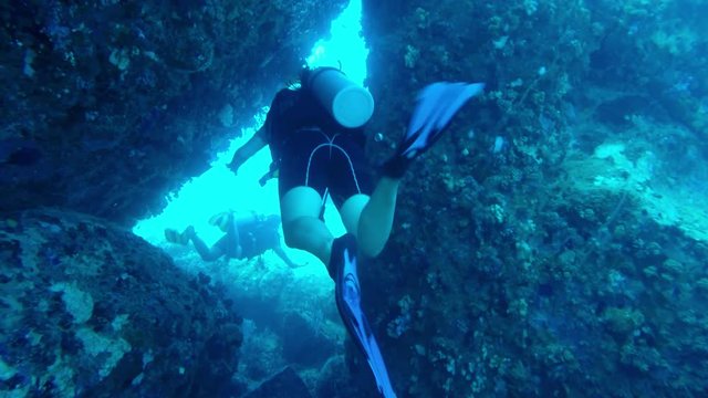 A female diver swims through a small opening in the rocks on a dive in the Seychelles