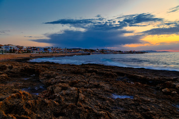 incredible sunset over the coast of Crete with hotels and beaches on the shore. Volcanic rock in the foreground