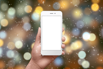 White smart phone ih hand surrounded with Christmas lights and bokeh. Isolated screen for mockup.