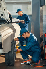 Service worker fixing a wheel of a car with his partner working in the background