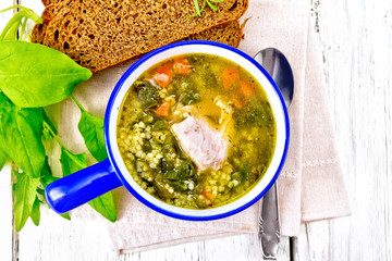 Soup with couscous and spinach in blue bowl on board top
