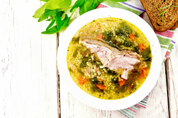 Soup with couscous and spinach in plate on light board top