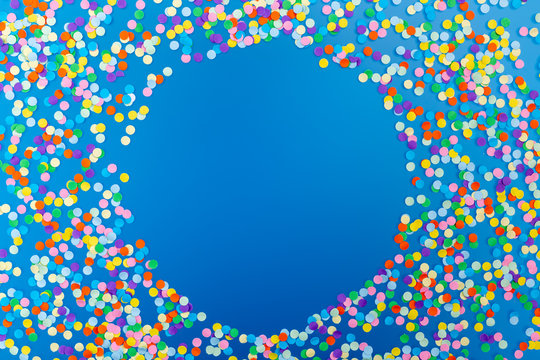 Round frame of colorful confetti on blue background.