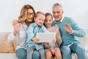 grandchildren and grandparents waving by hands while having video call with digital tablet at home