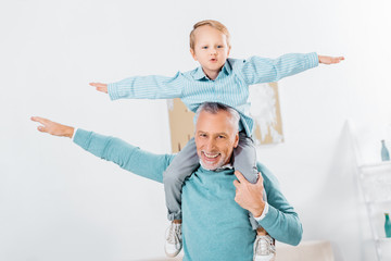 child sitting on happy grandfather shoulders and imitating plane at home