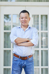Portrait of Asian handsome man standing with arms crossed with beautiful house in the background