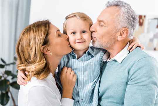 happy middle aged couple holding adorable grandson and kissing him in cheeks