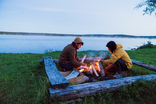 Sweden, Lapland, Two friends preparing a bonfire at the lakeshore