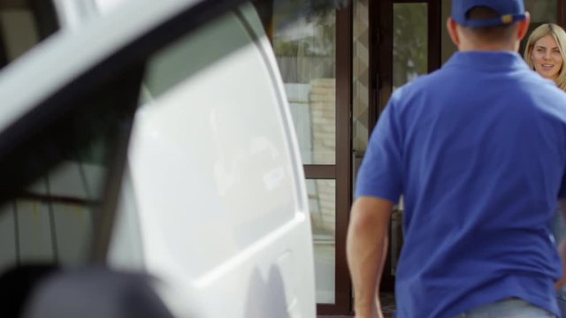 PAN shot of male courier in blue uniform getting out of delivery van and taking packages for shipping from happy woman standing on doorstep