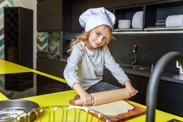 Little girl with chef hat, rolling pin preparing dough, bake homemade holiday apple pie in kitchen....