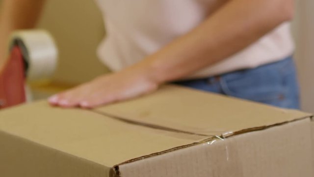 Close up shot of unrecognizable woman sealing cardboard box with duct tape
