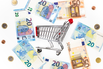 Empty shopping cart with around various banknotes and metal money