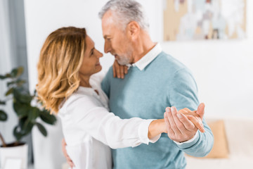 selective focus of mature couple dancing face to face at home