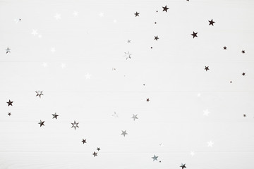 Holiday backdrop made of silver stars and sparkles on white wooden background. New Year concept.