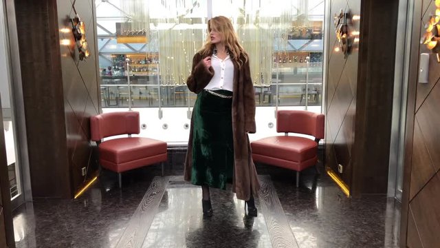 Young slim blonde woman in mink coat posing in the lobby of an expensive hotel