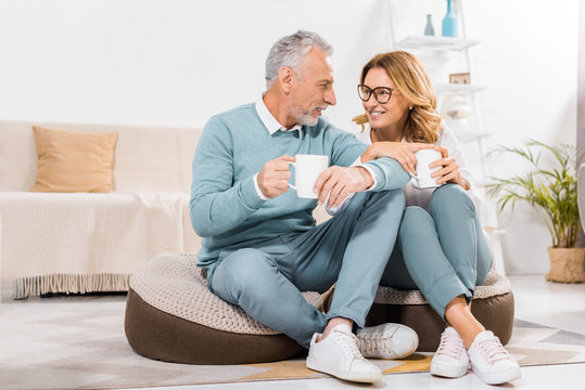 Middle Aged Couple Sitting With Cups Of Coffee In Living Room At Home