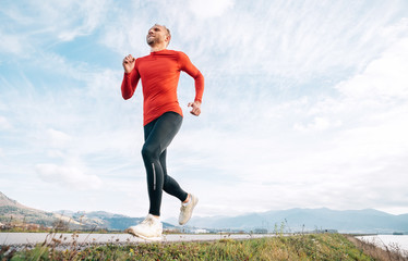 The wide angle shoot of a Man dressed in red long sleeve shirt runs by the road with mountain...