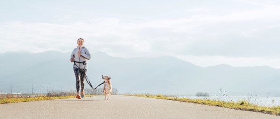Heldere zonnige ochtend Canicross-oefeningen. Vrouw loopt met zijn beagle hond en gelukkig lachend.