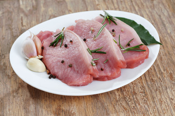 Raw sliced pork meat prepare with pepper rosemary garlic and bay leaves in white plate on old wooden table