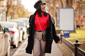 African american fashion girl in coat and newsboy cap posed at street.