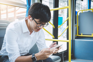 Young Asian man traveler sitting on a bus using smartphone watch video or playing game while smile...