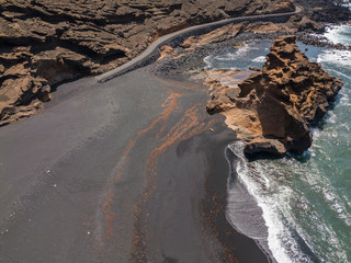 Vista aerea di una strada pedonale che costeggia la costa frastagliata di Lanzarote, isole Canarie, Spagna. Charco de los Clicos. Onde che si infrangono su scogli e massi. Sabbia nera. Playa El Golfo